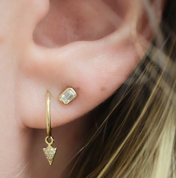 Close-up of an ear wearing gold hoop earrings with gemstones.