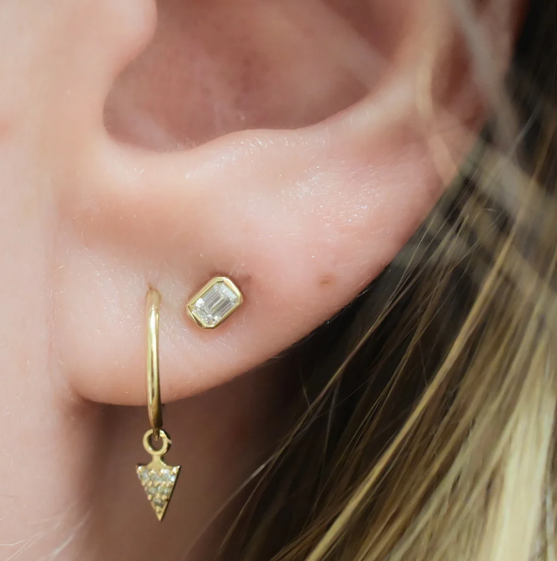Close-up of an ear wearing gold hoop earrings with gemstones.