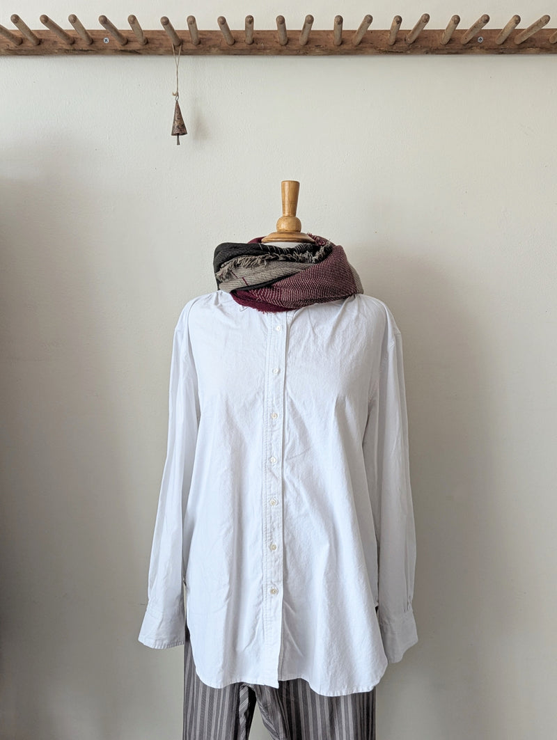 White shirt on a mannequin with a scarf draped over it against a plain wall.