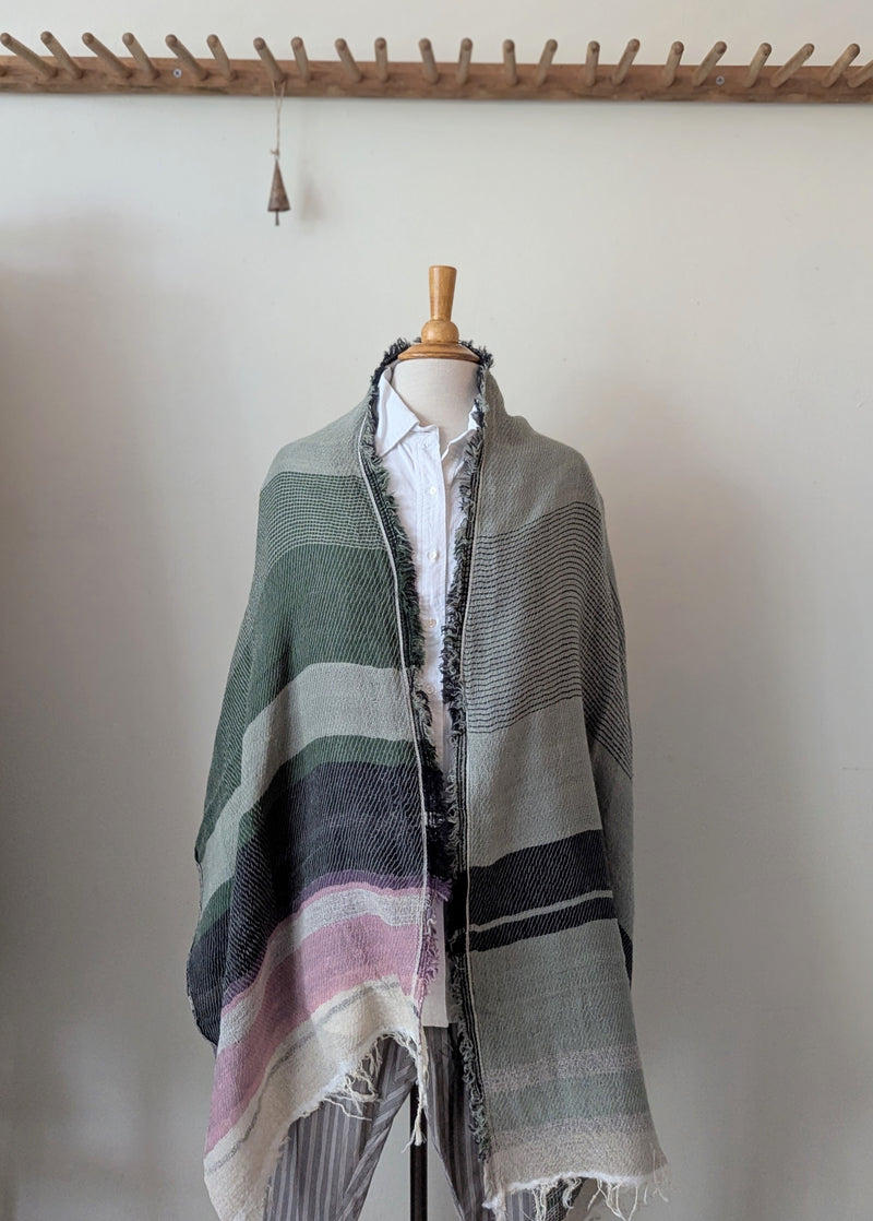 Mannequin wearing a green and gray striped poncho with a white shirt underneath against a plain background.