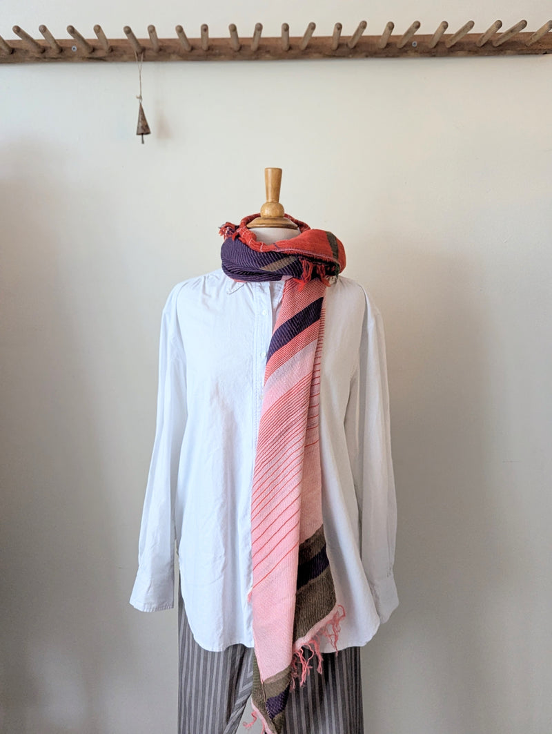 Mannequin wearing a white shirt with a colorful scarf draped over it against a plain wall.