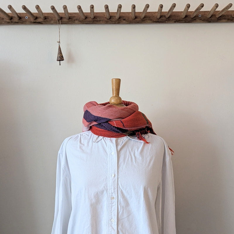 Mannequin wearing a white shirt with a red and purple scarf draped over it, against a plain wall.