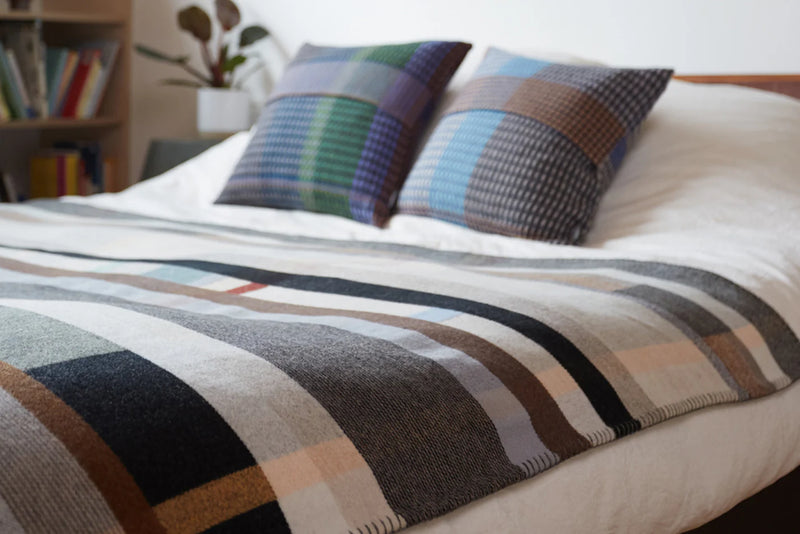 Bed with plaid blanket and patterned pillows in a room setting.