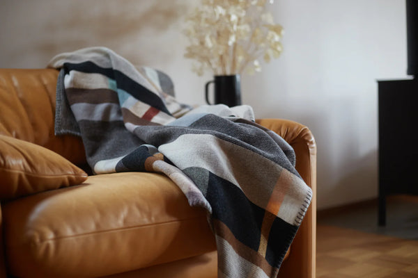 Plaid blanket draped over a brown leather sofa with a blurred background