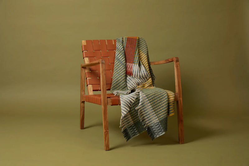 Wooden chair with woven armrests draped with a patterned blanket on a plain background