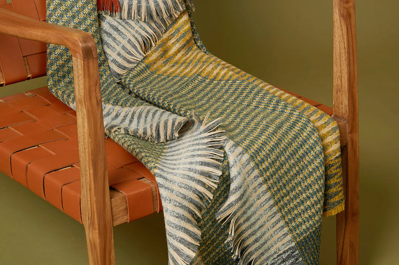 Woven blanket draped over a wooden chair with a green background