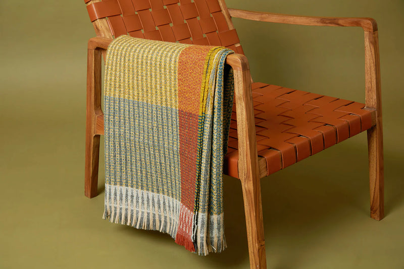 Woven blanket draped over a wooden chair against a green background