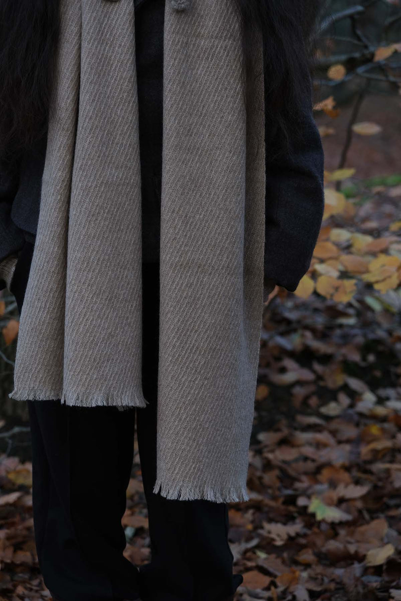 Person wearing a long beige scarf with a blurred autumn background