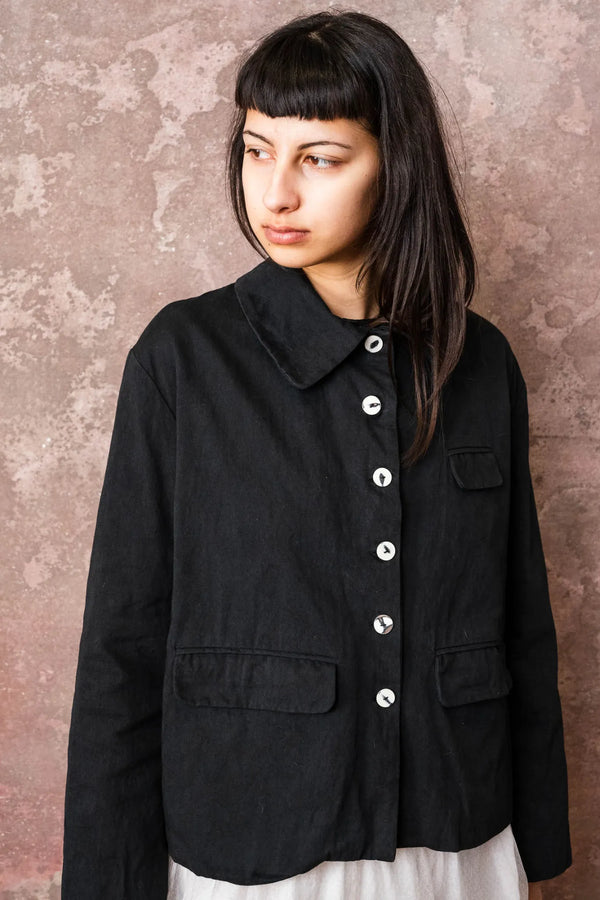 Woman wearing a black jacket with white buttons against a textured wall.