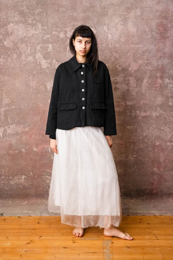 Person wearing a black jacket and white skirt against a textured wall.