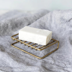 Bar of soap on a brass soap stand with a soft gray fabric background.

Fog Linen brass bar soap stand bath shower home decor kitchen Boston gift shop store boutique