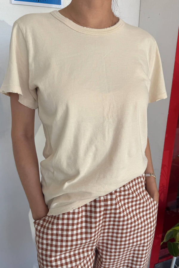 Person wearing a beige t-shirt and red checkered pants against a plain background