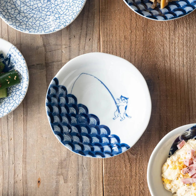 White ceramic bowl with blue wave pattern and cat fishing illustration on a wooden table.