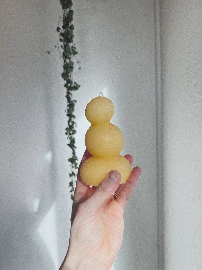 Hand holding a yellow three-bulb candle against a neutral background