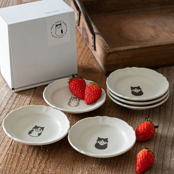 Set of small white plates with cat illustrations on a wooden surface with strawberries.