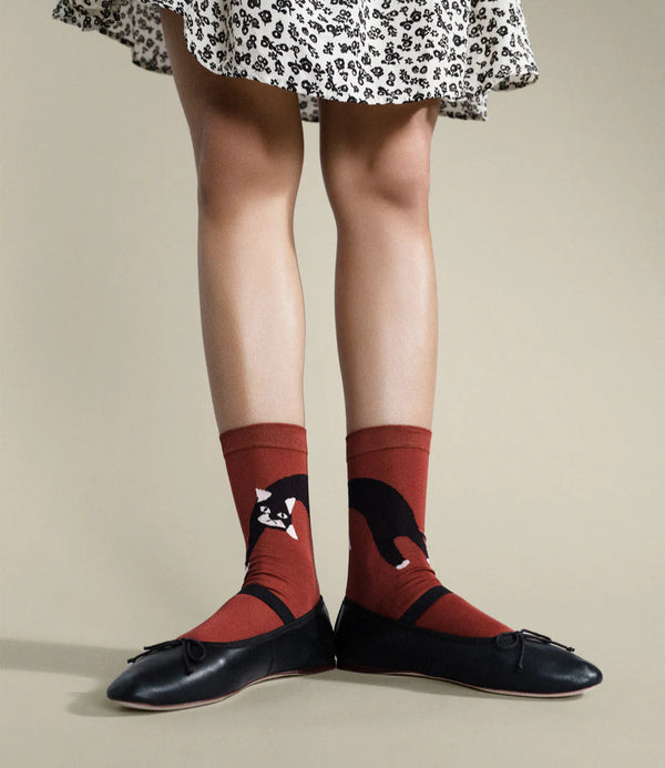 Person wearing a floral skirt, red socks with black accents, and black shoes on a beige background