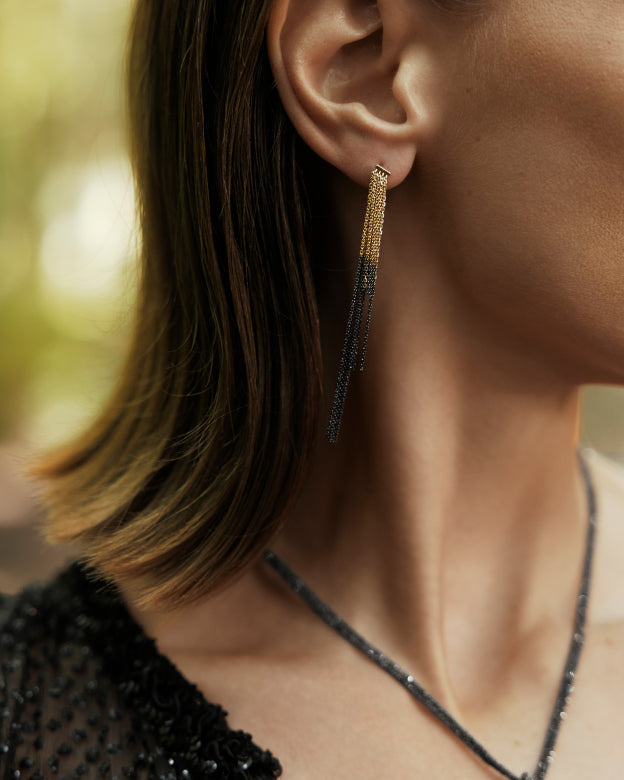 Close-up of a person wearing gold chain earrings with black accents.