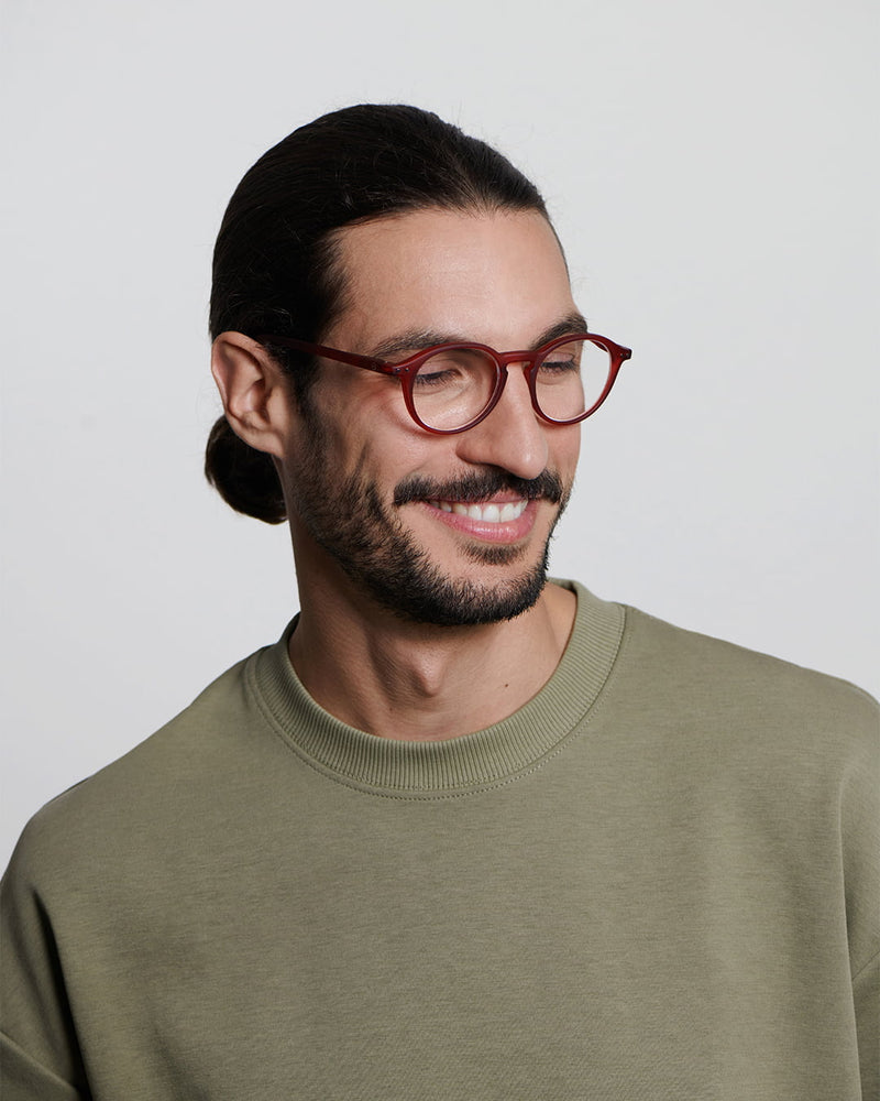 Man wearing red glasses and a green sweater against a plain background