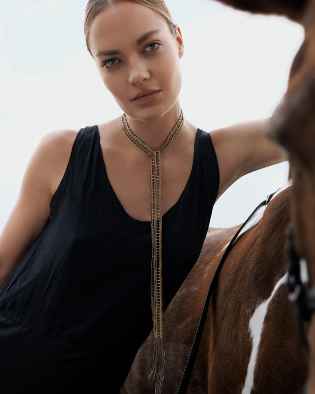 Woman wearing a long necklace with a horse in the background