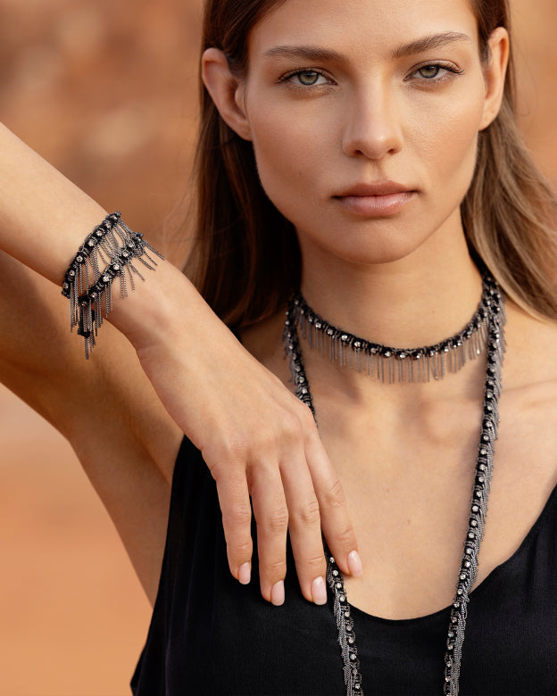 Woman wearing a black fringe necklace and bracelet against a neutral background