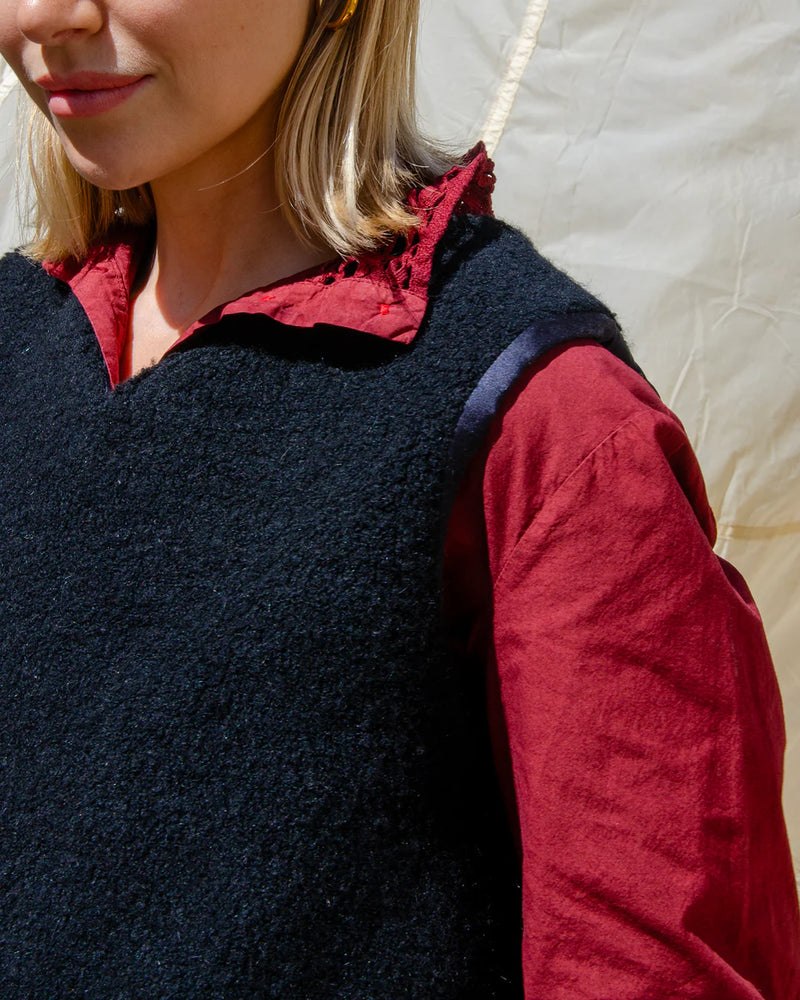 Person wearing a dark black wool vest over a red shirt with a neutral background