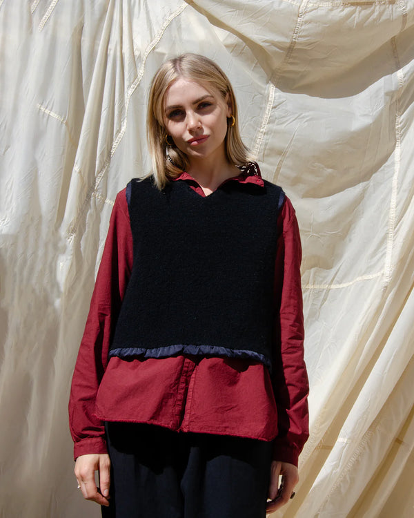 Woman wearing a red shirt with a black vest against a textured white background