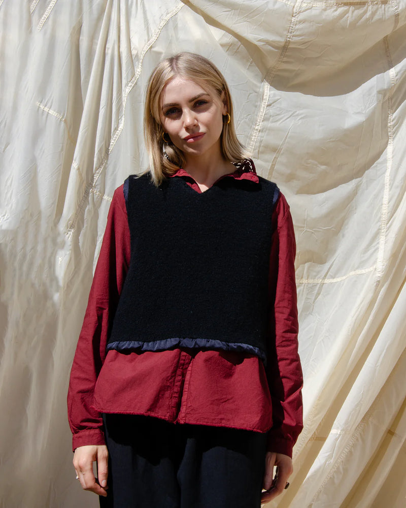 Woman wearing a red shirt with a black vest against a textured white background
