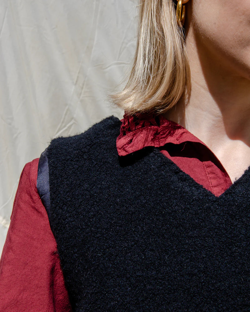Person wearing a black vest over a red shirt with a plain background