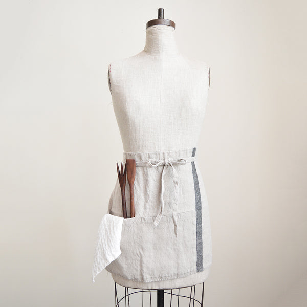 Half apron made of heavy weigh linen. An offset stripe and a large pocket divided in two make this utilitarian apron a durable and stylish kitchen companion.  