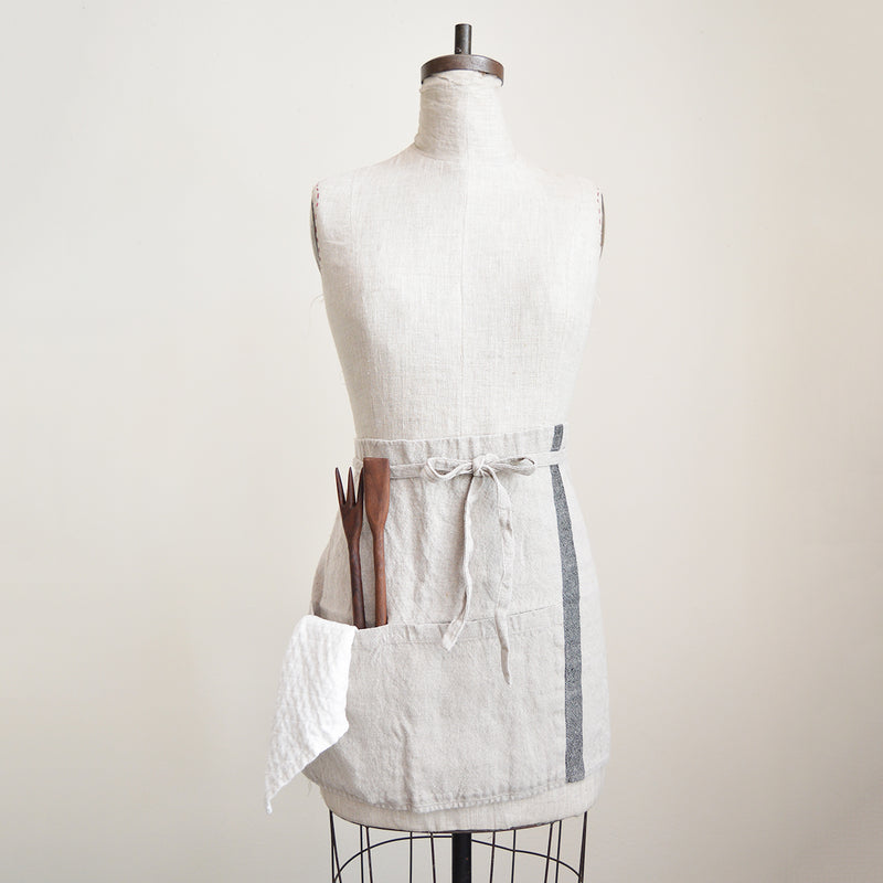 Half apron made of heavy weigh linen. An offset stripe and a large pocket divided in two make this utilitarian apron a durable and stylish kitchen companion.  