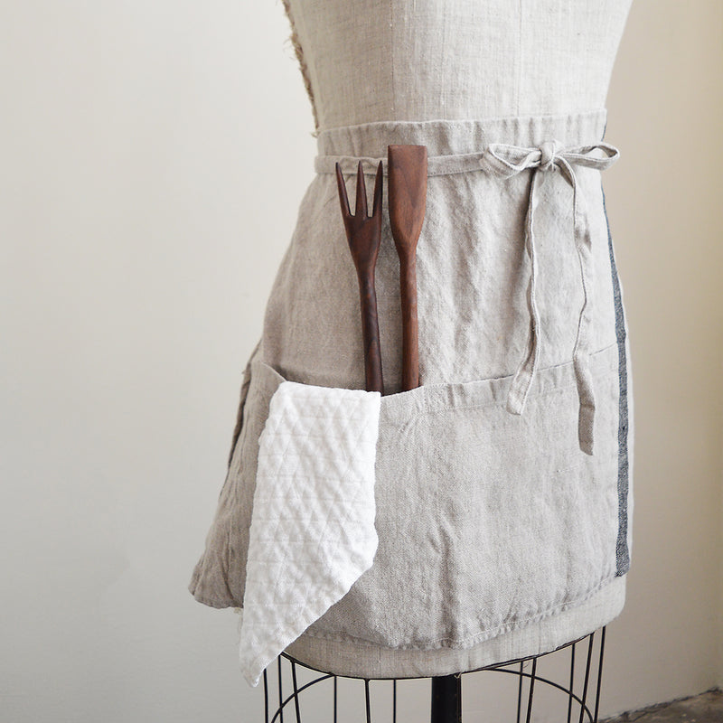 Half apron made of heavy weigh linen. An offset stripe and a large pocket divided in two make this utilitarian apron a durable and stylish kitchen companion.  