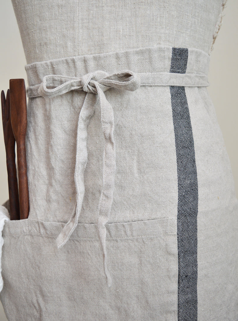 Half apron made of heavy weigh linen. An offset stripe and a large pocket divided in two make this utilitarian apron a durable and stylish kitchen companion.  