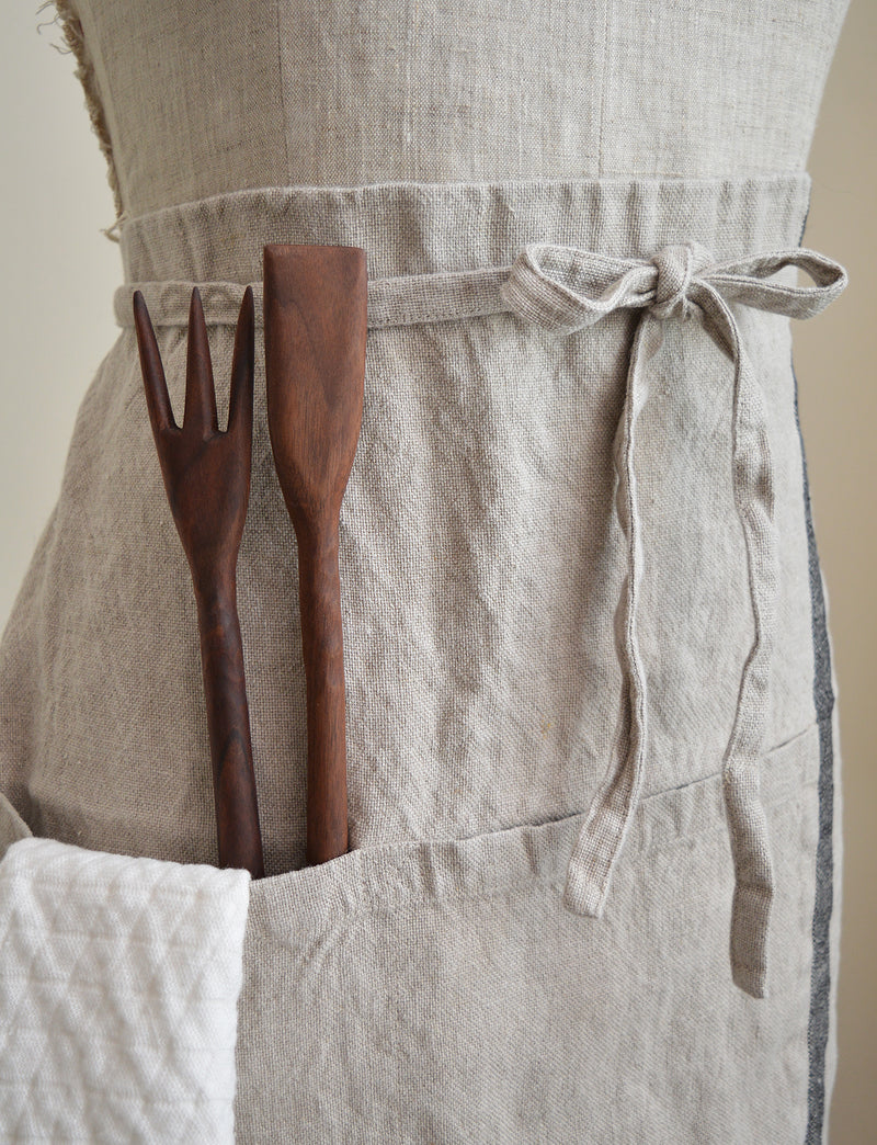 Half apron made of heavy weigh linen. An offset stripe and a large pocket divided in two make this utilitarian apron a durable and stylish kitchen companion.  